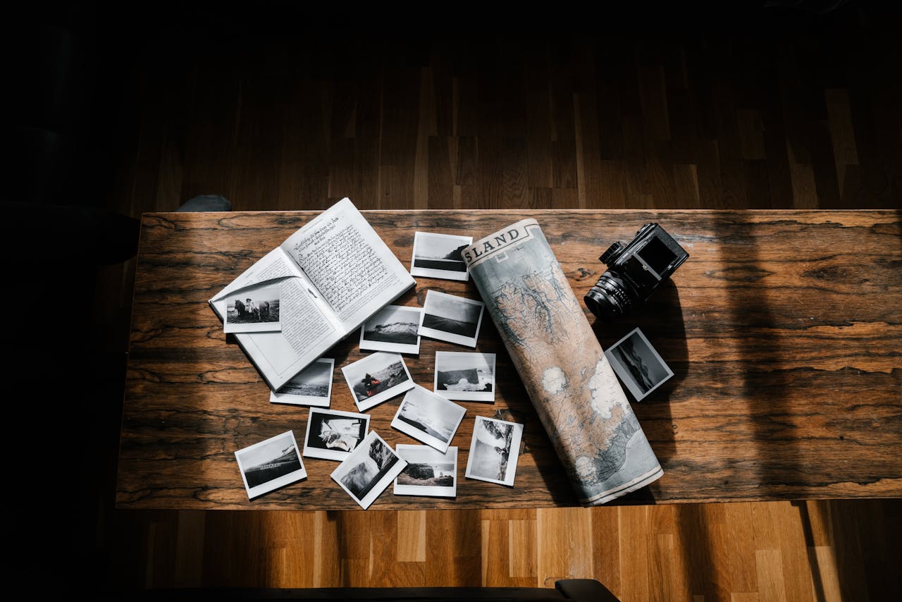 A nostalgic arrangement of a journal, photos, camera, and map on a wooden table, evoking travel memories.